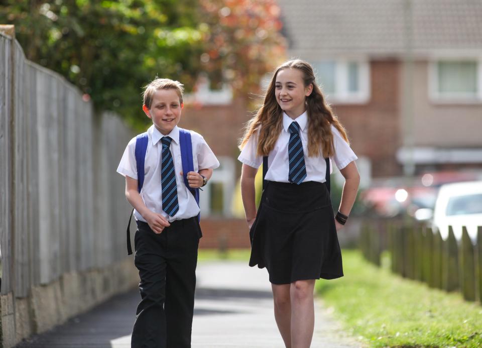Two school children in uniform walking down a sidewalk.