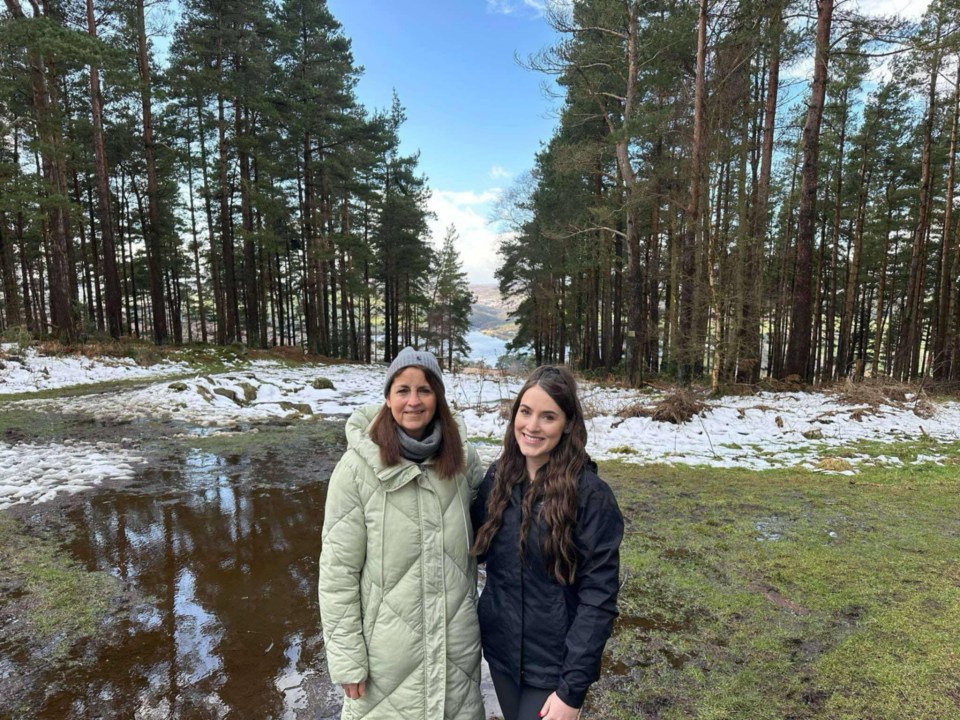 A mother and daughter stand in a snowy forest clearing.
