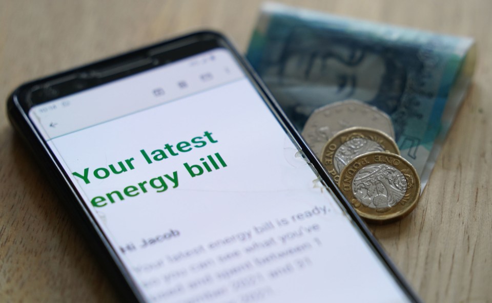 Smartphone displaying an energy bill notification next to British currency.