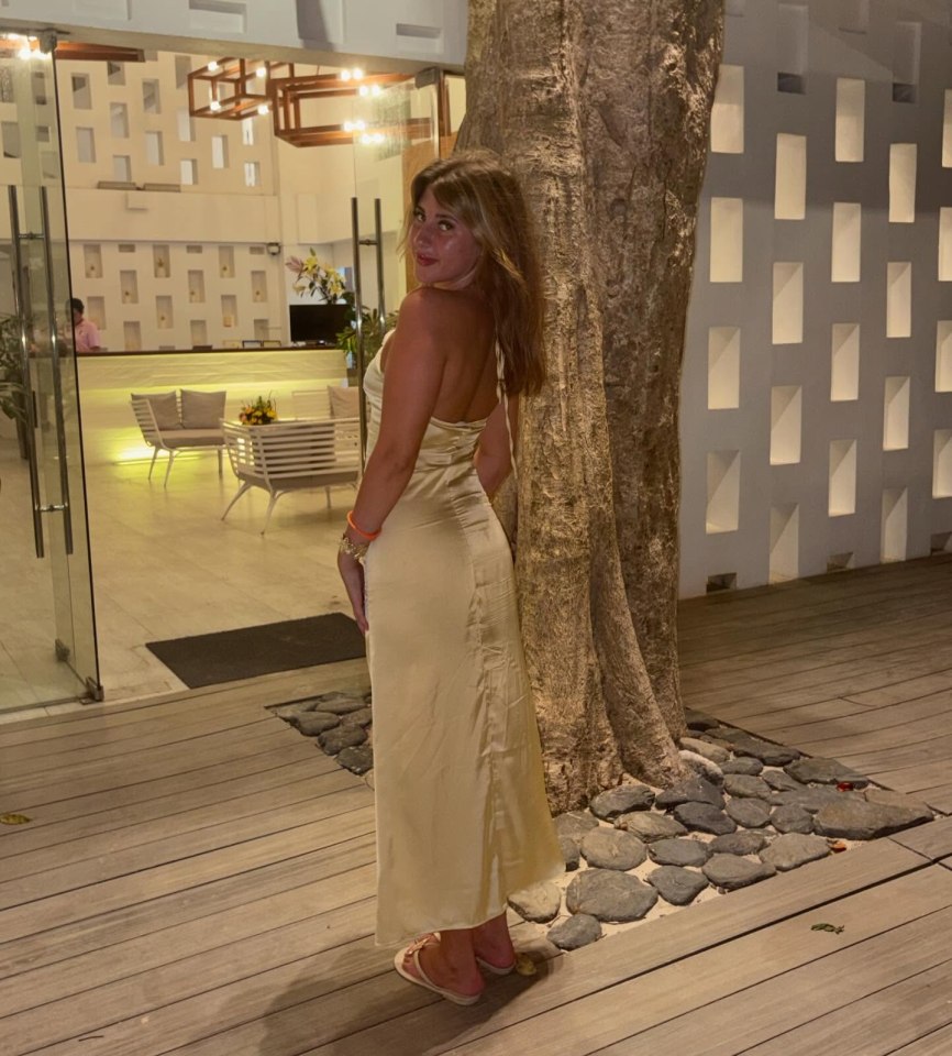 Woman in a beige dress standing outside a hotel.
