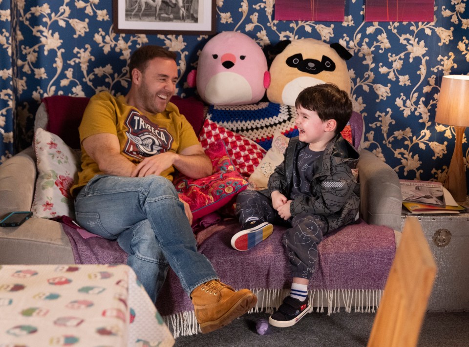 Tyrone Dobbs and a young child sit on a couch together.