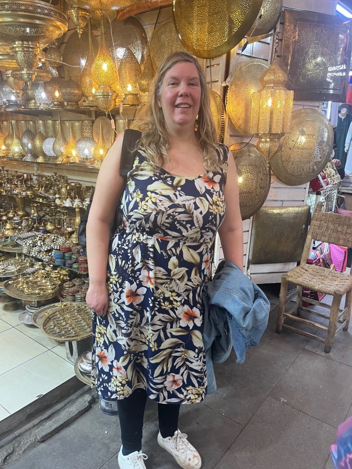 Woman in floral dress in Marrakesh market surrounded by brass lamps.