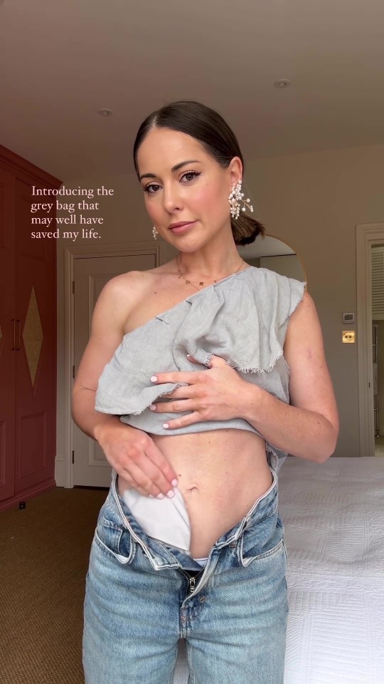 Woman showing a small grey bag in her waistband, stating that it may have saved her life.