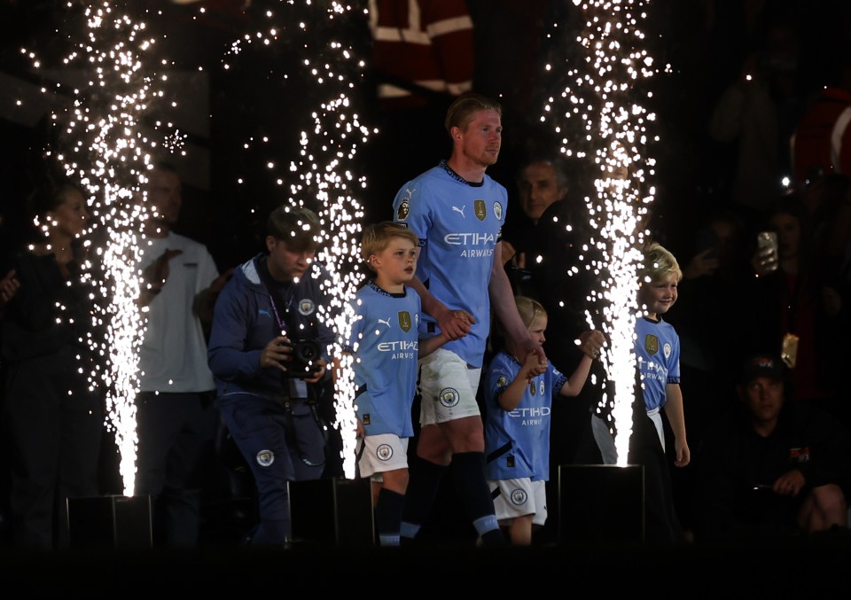 Kevin De Bruyne with children in Manchester City jerseys, surrounded by fireworks.
