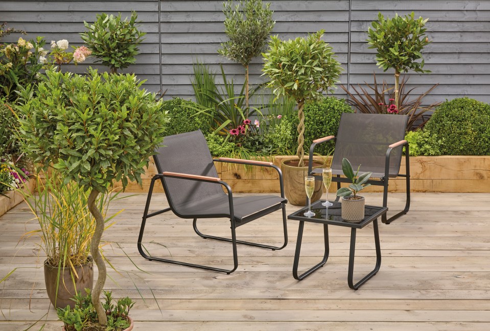 Two black metal and fabric patio chairs and a small table on a deck, surrounded by potted plants.