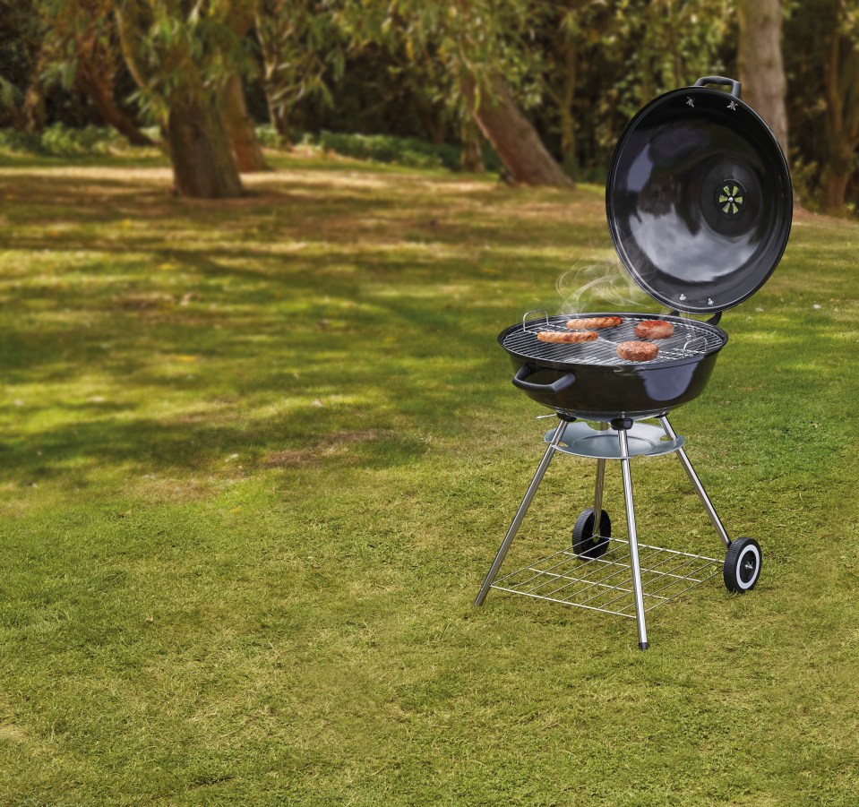 Kettle barbecue with sausages and burgers cooking on a lawn.