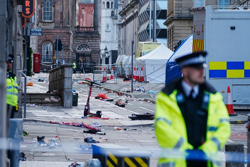 Debris-strewn street scene with police tents and officers following a car crash.