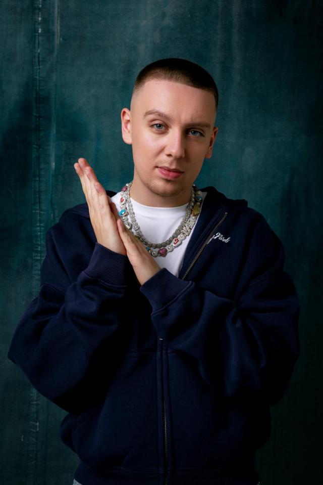 Portrait of Aitch wearing a navy zip-up hoodie and multiple necklaces.