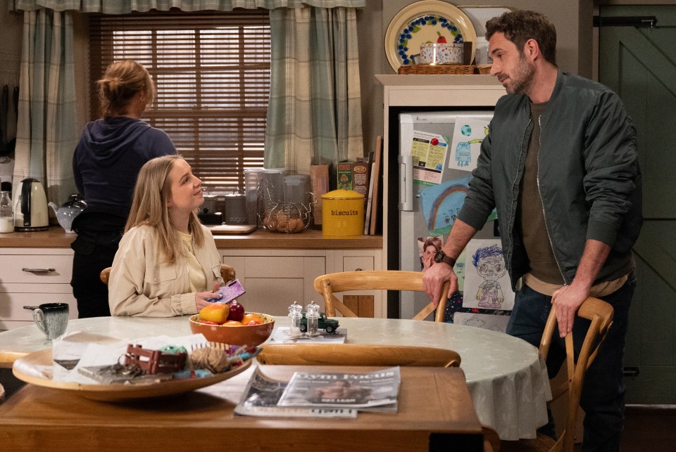 Scene from Emmerdale showing John Sugden and Belle Dingle in a kitchen.