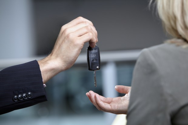 A car salesman handing car keys to a woman.