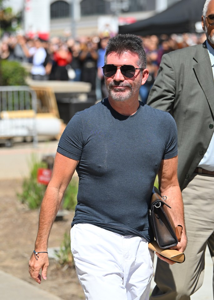 Simon Cowell walking outdoors, carrying a bag.