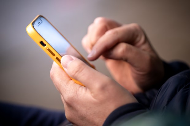 Close-up of a man's hands using a yellow smartphone outdoors.