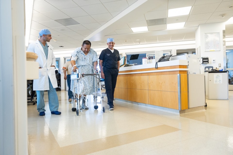 A transplant recipient walks down a hospital hallway with two doctors.