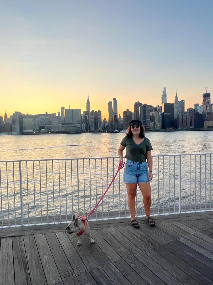 Woman walking a dog with the NYC skyline in the background.