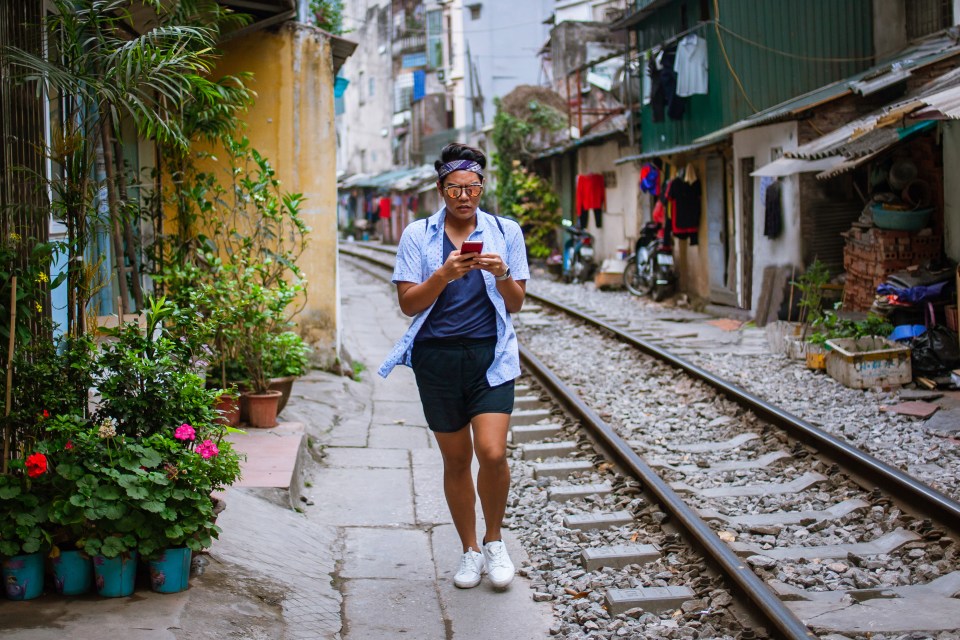 Person walking down a train track in Hanoi's Old Quarter, using a smartphone.