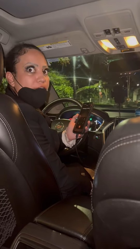 A frightened woman in a car uses her phone to call emergency services.