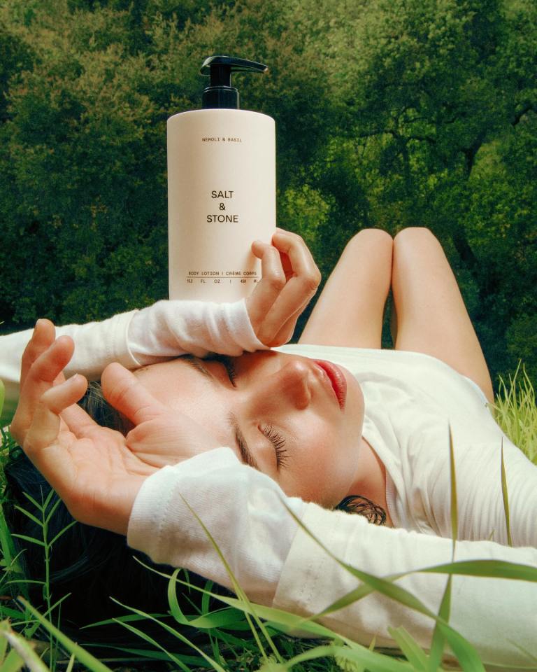 Person lying in grass holding Salt & Stone body lotion.