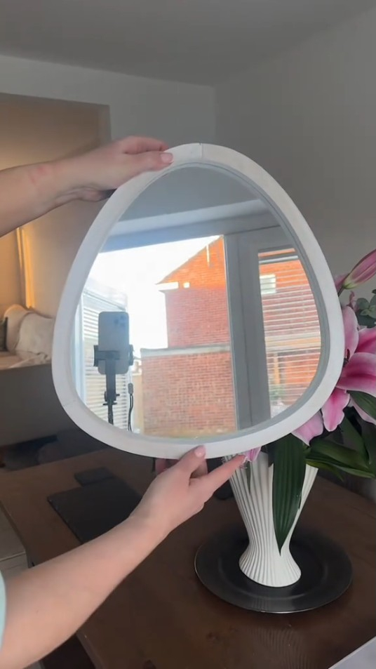 Person holding up an oval white framed mirror.