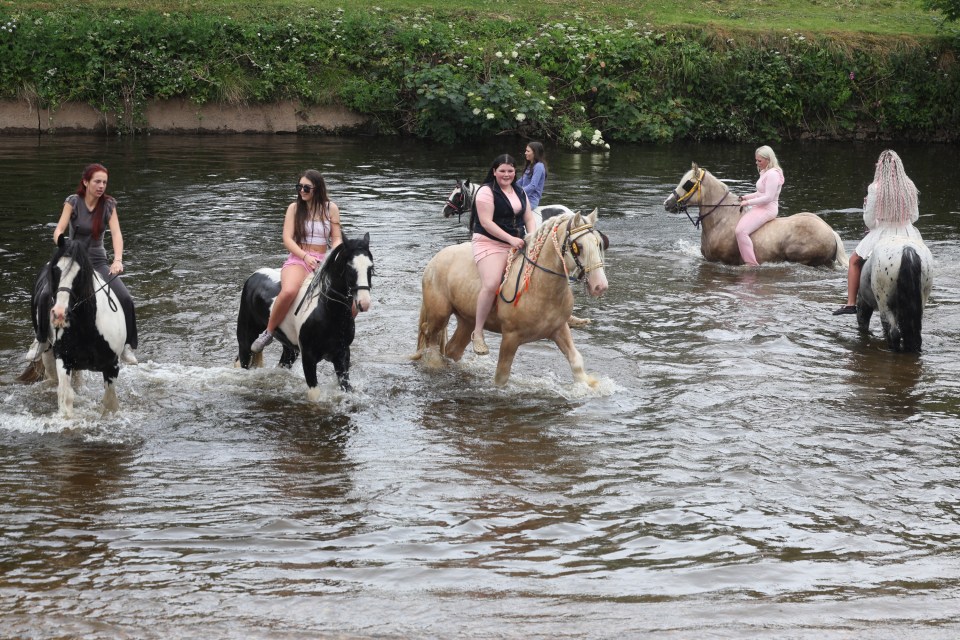 Travellers riding horses through a river at the Appleby Horse Fair.