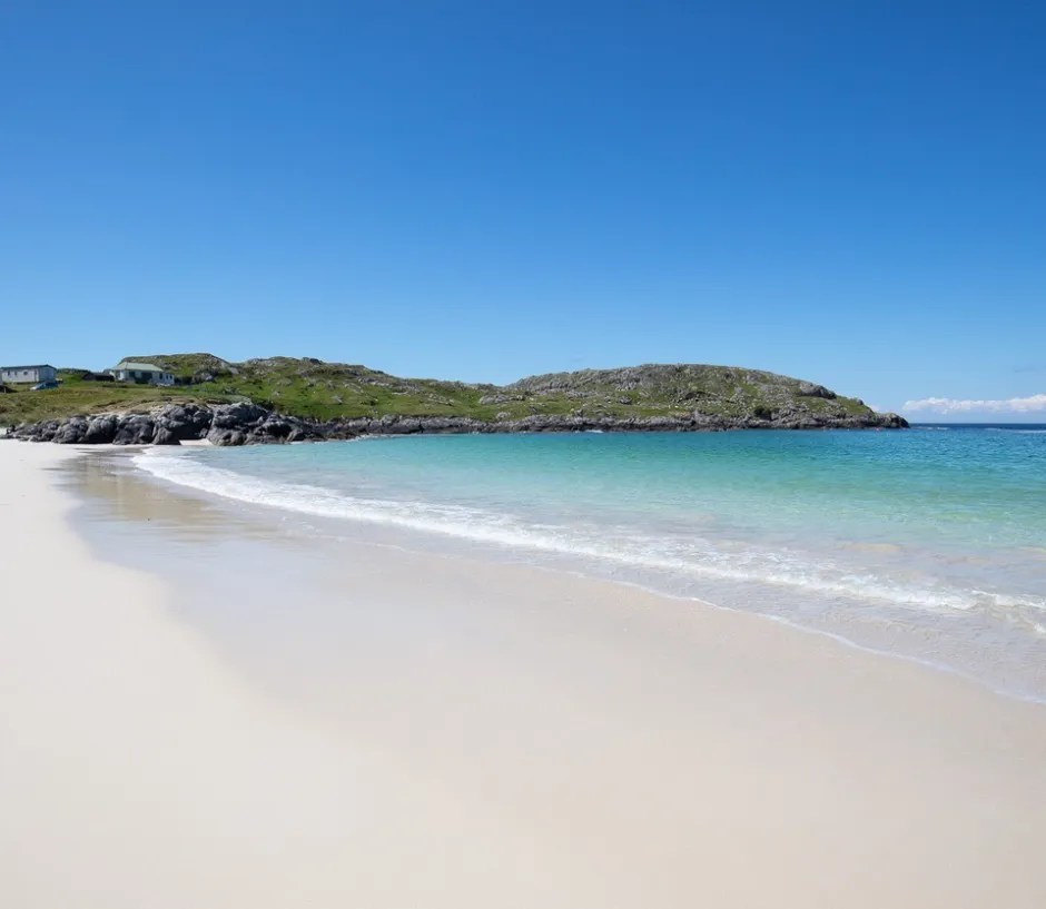 White sand beach and turquoise water with a small hill in the background.