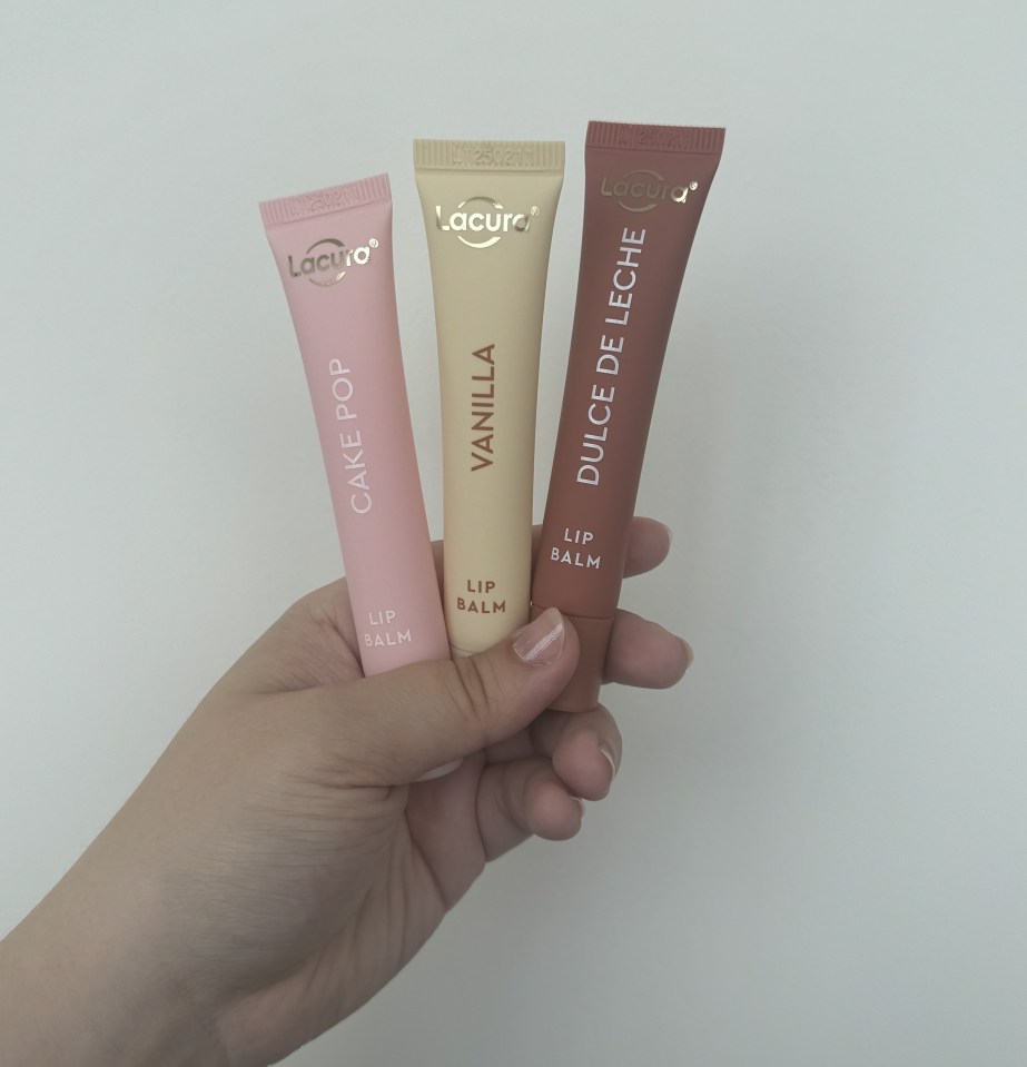 Hand holding three tubes of Lacura lip balm in Cake Pop, Vanilla, and Dulce de Leche.