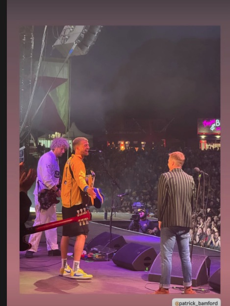 Three men on stage at a concert in front of a large crowd.