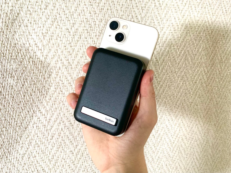 Hand holding a Belkin magnetic charger attached to a smartphone.