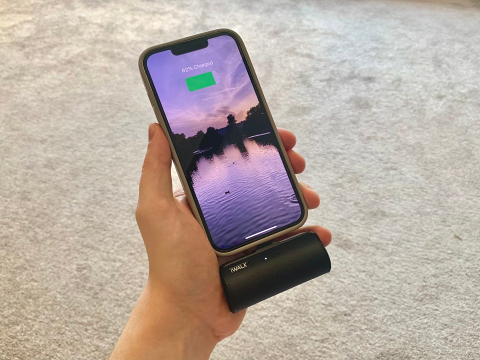 A hand holding a smartphone that is 82% charged using an iWalk power bank.
