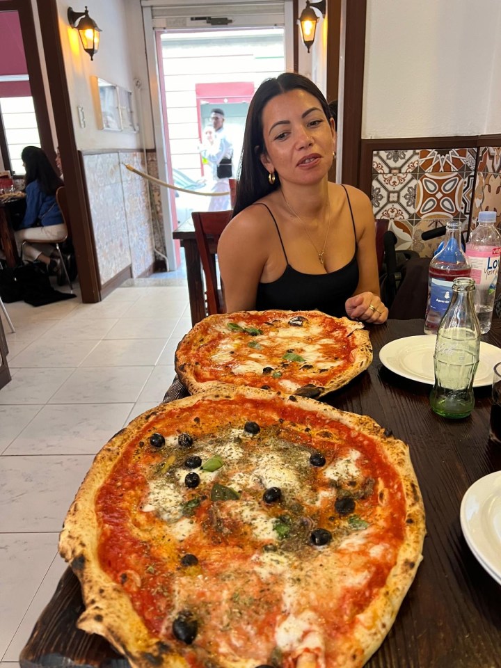Woman sitting at a table with two large pizzas.