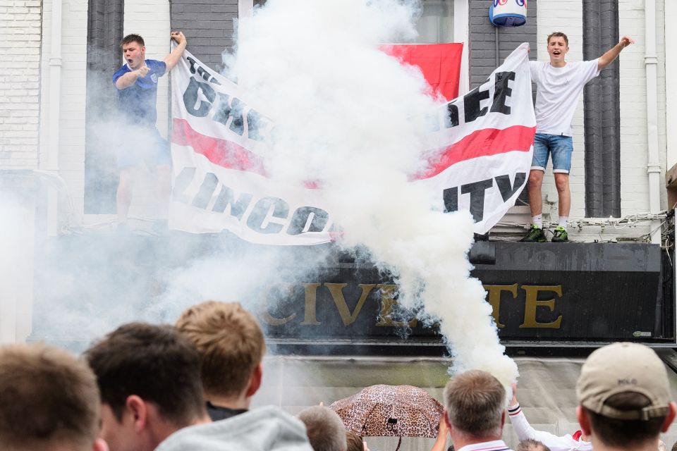 A flare is ignited as England fans hang a flag onto a bar's canopy in central Lens