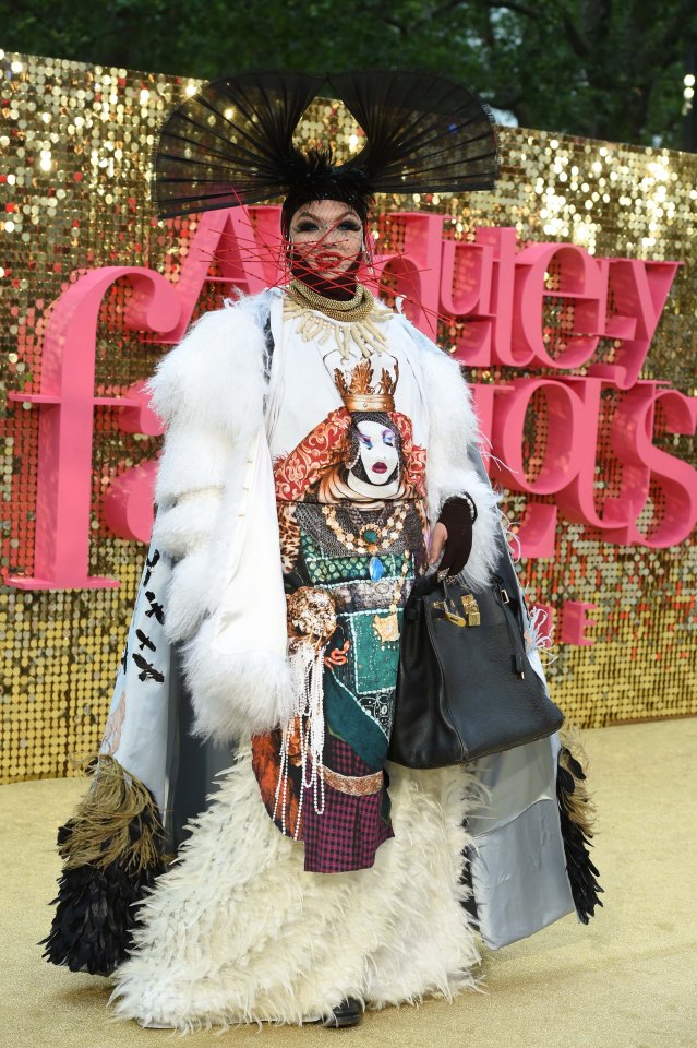A drag queen takes to the red carpet in a white fluffy coat