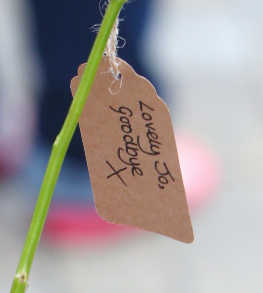 A touching handwritten note hanging from flowers which says 'Lovely Jo, goodbye x'