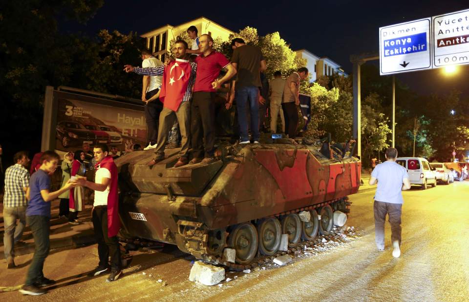 Supporter of Turkish President Tayyip Erdogan stand on an abandoned tank outside parliament building in Ankara