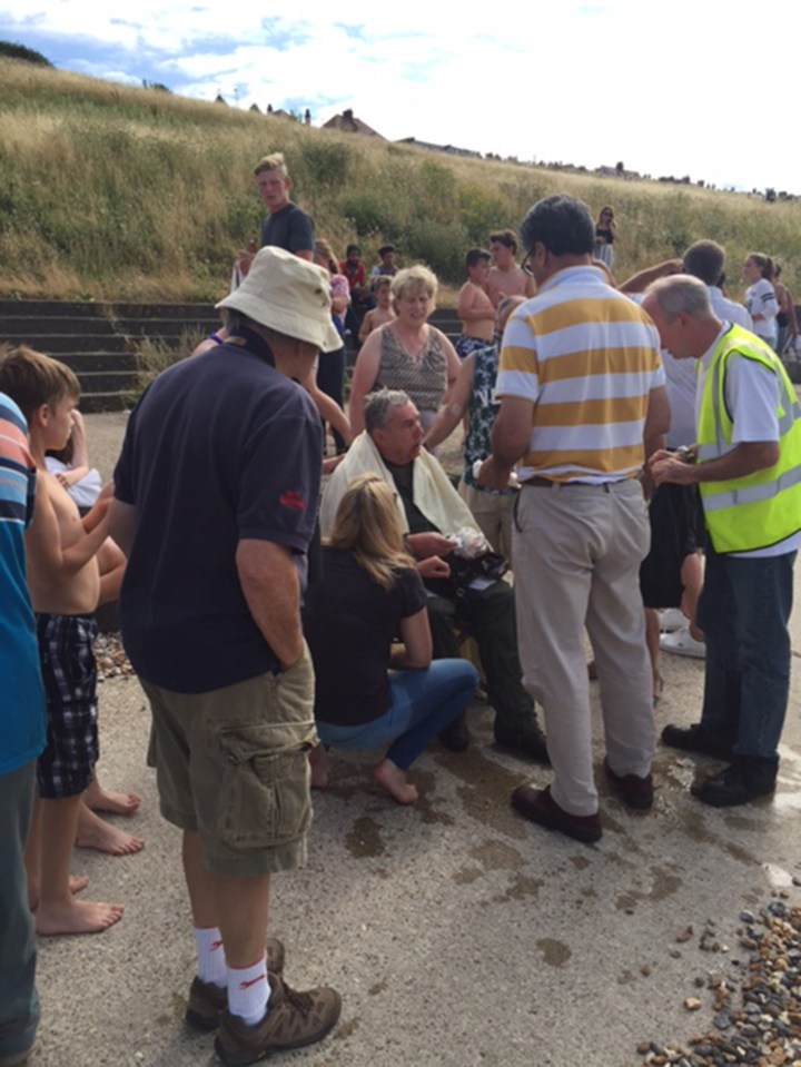 Spectators surround the injured pilot who looks bloodied and bruised just moments after being pulled from the water