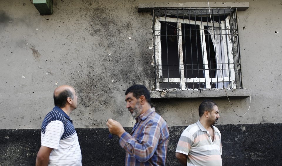 People stand below a shattered window that was damaged during a bomb attack