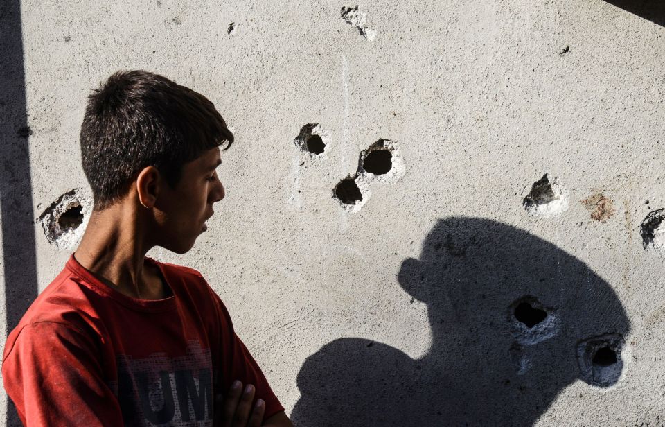 A boy stands near impacts of projectile on a wall near the explosion scene 