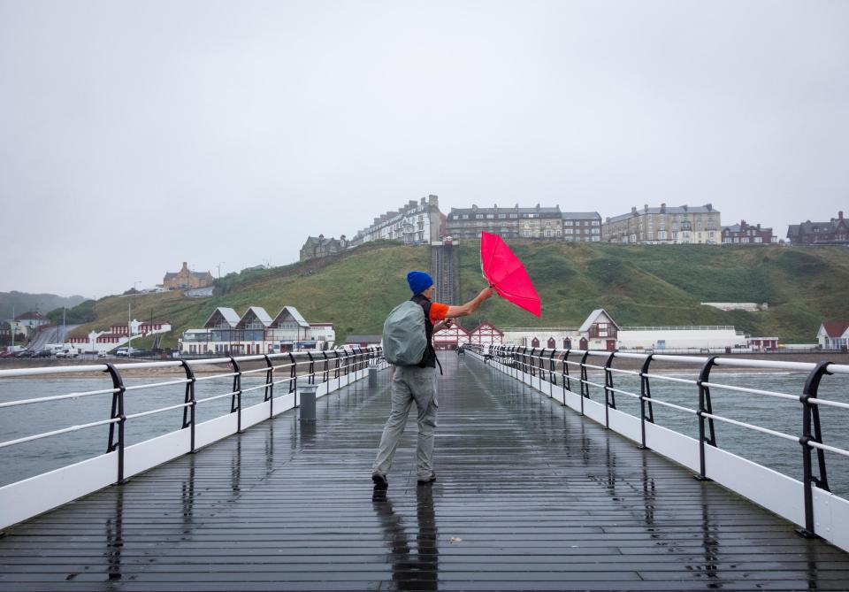 A hiker walking the Cleveland Way National trail on Saltburn`s Victorian pier struggles with his brolly