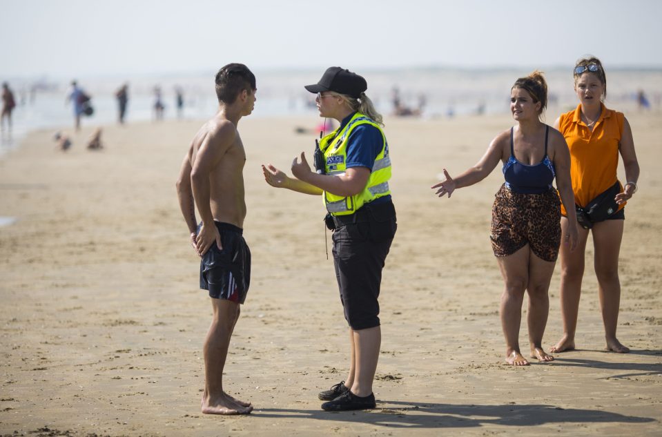 A police officer advises a swimmer to come in as the tide moves in on Camber Sands where five people lost their lives last night