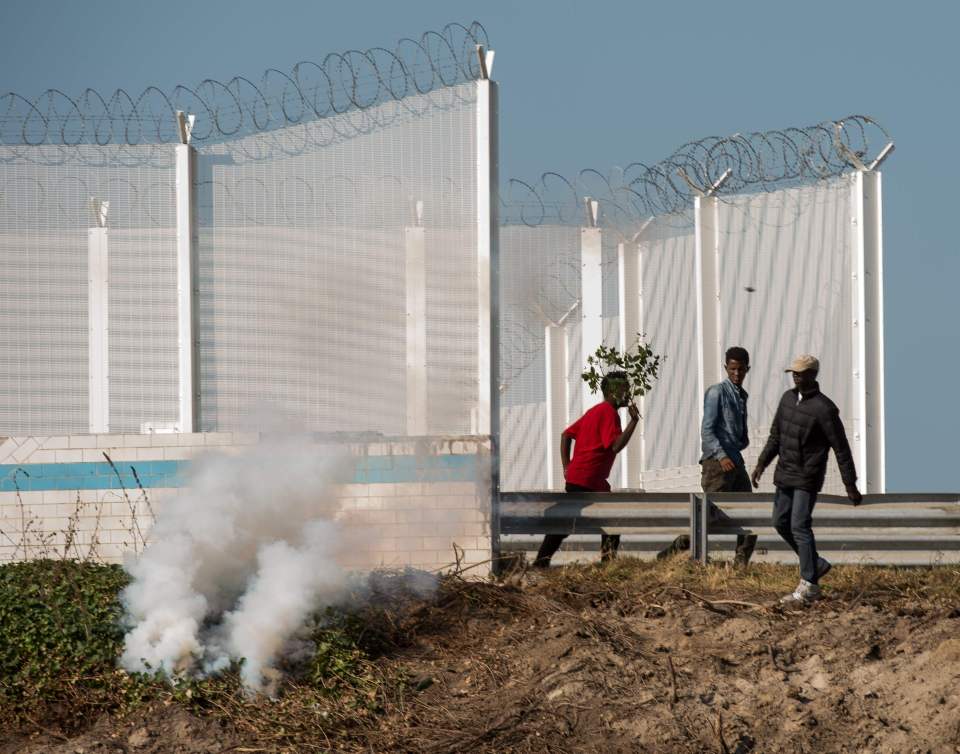 Migrants flee from a tear gas canister fired by cops