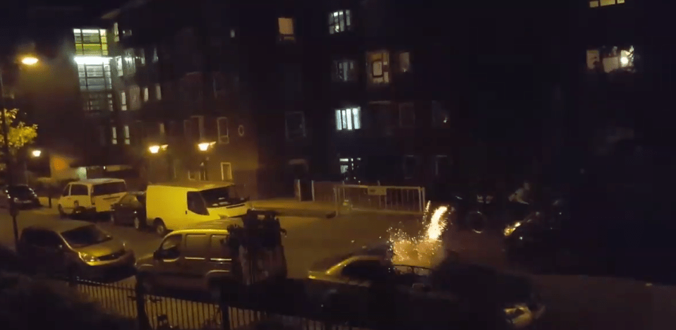 The fireworks can be seen to ricochet off parked cars with the gang running around the streets late Saturday night