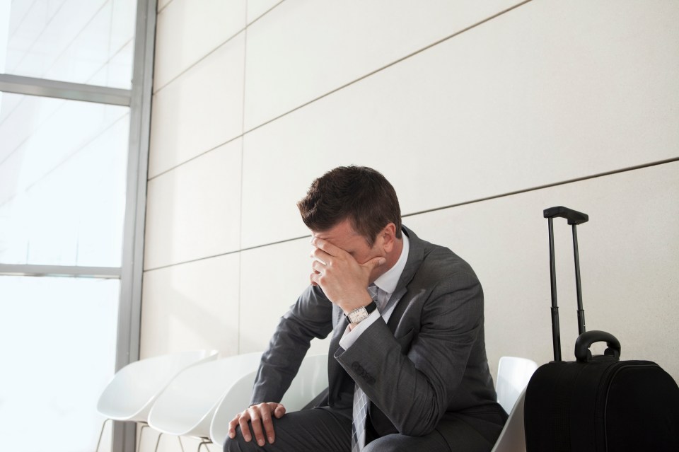 Businessman waiting with luggage, head in hands