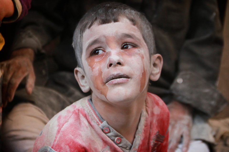Tears stream down the face of a child covered in dust and blood