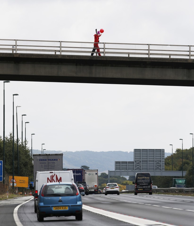 FAMEFLYNET - Exclusive: The Killer Clown Craze Shows No Sign Of Slowing Down As An Individual Dressed As A Clown Brandishing A Sword Is Seen On A Bridge Taunting Traffic Below On The M20