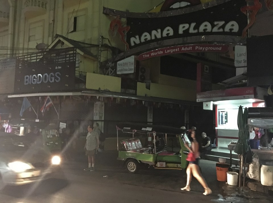 People walk past Bangkok's Nana Plaza red-light district, after it closed down temporarily following the death Thursday of Thailands 88-year-old King Bhumibol Adulyadej