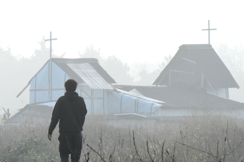 A migrant walks past a makeshift church in the "Jungle" migrant camp 