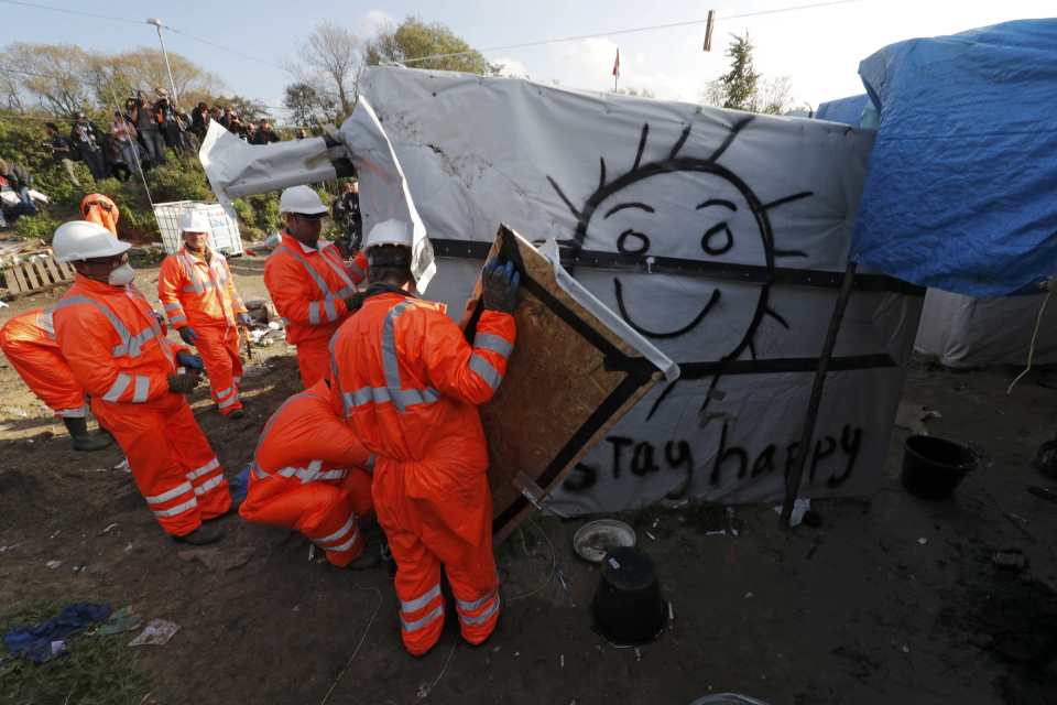 Workers in orange jumpsuits began work on dismantling smaller structures ahead of the arrival of heavy machinery