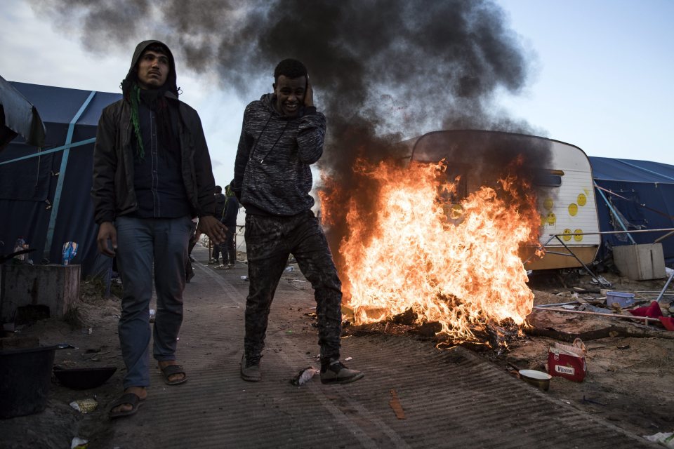 Migrants walk next to a fire caused by other migrants