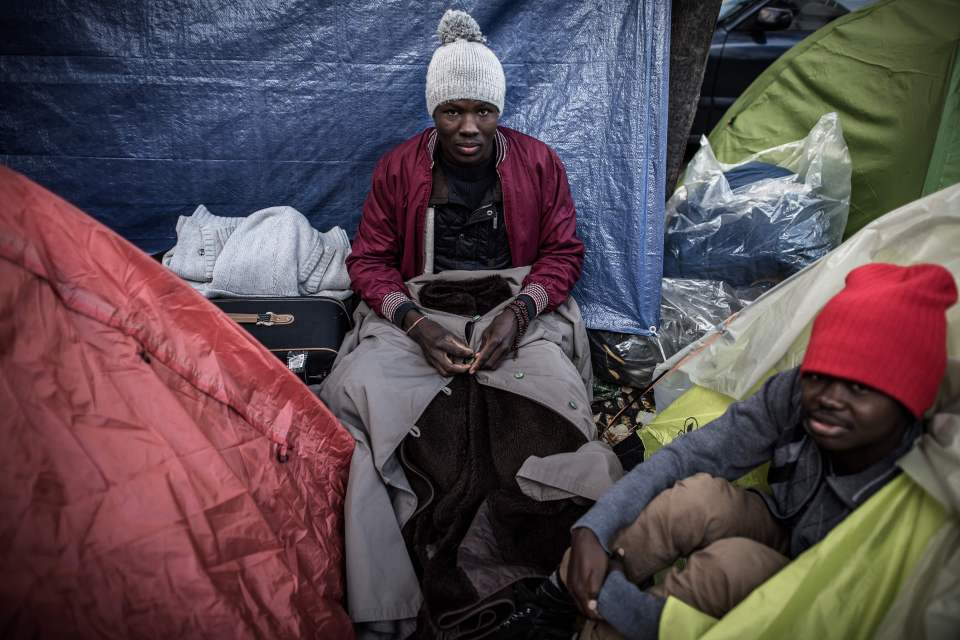 Migrants sit outside their tents in one of the growing new camps in the capital
