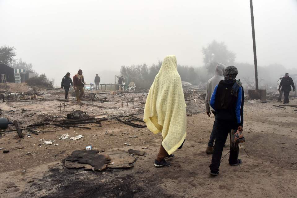  Migrants walk among the remains of burnt makeshift shelters at the 'Jungle' migrant camp in Calais