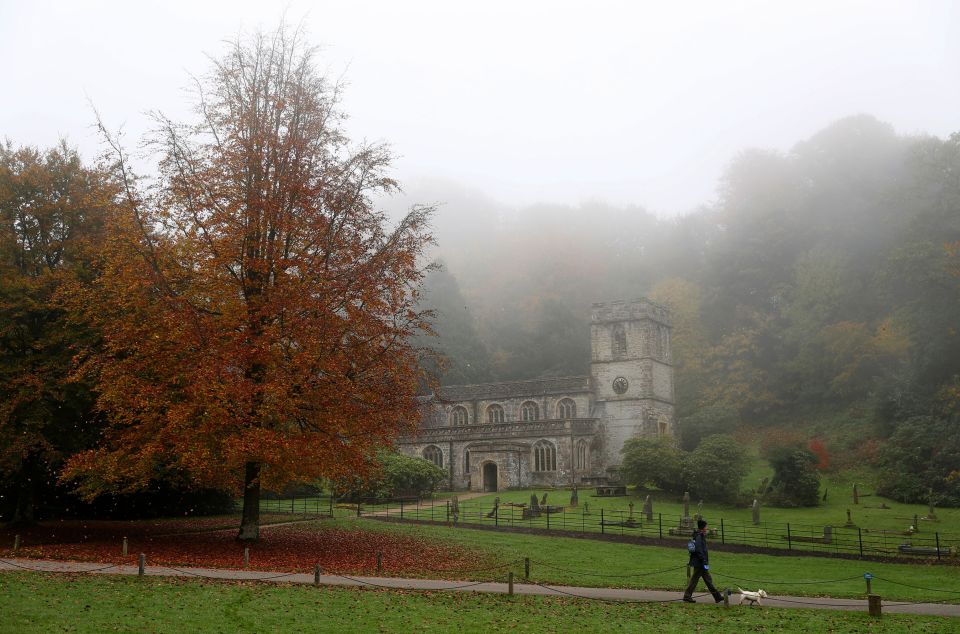 A fog descends as a man walks a dog past St Peter's Church in Stourhead, Wiltshire